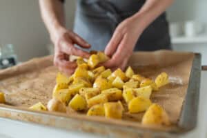 Woman preparing fresh, raw and chopped potatoes on a baking sheet for making roasted potatoes