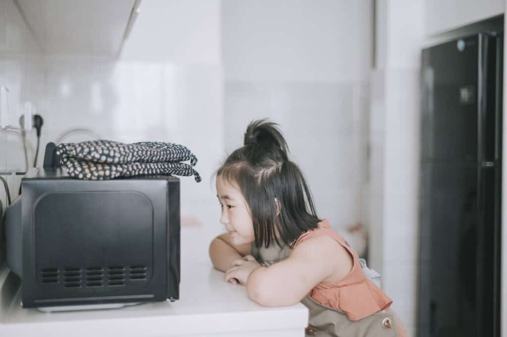 Young girl waiting for potatoes to cook in the microwave.