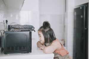 Young girl waiting for potatoes to cook in the microwave.