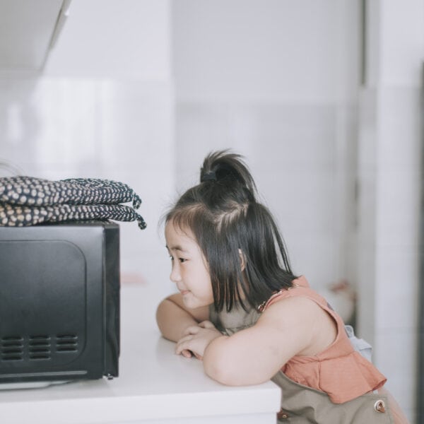 Young girl waiting for potatoes to cook in the microwave.